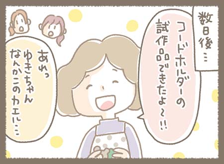 数日後、ゆきちゃんがエプロン姿で完成したコードホルダーの試作品を手にしながら「できたよ」と見せ、そばにいるみなちゃんとまきちゃんも興味深そうに様子を見ている。